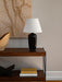 The Torso Table Lamp, 57, styled on a dark wood console table with books, a decorative bowl, and textured wall art behind it.