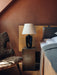 The black Torso Table Lamp, 57 on a marble plinth as a bedside lamp in a bedroom with a sheepskin chair and terracotta walls.