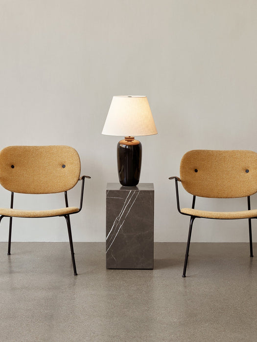 The Torso Table Lamp, 57, illuminated on a dark marble plinth, sits between two mustard-yellow upholstered chairs.