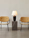 The Torso Table Lamp, 57, illuminated on a dark marble plinth, sits between two mustard-yellow upholstered chairs.