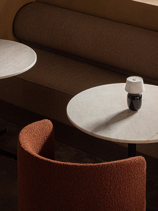 A Torso Portable Table Lamp on a marble Nook Dining Table, with a rust-coloured Tearoom Club Chair and a dark brown booth.