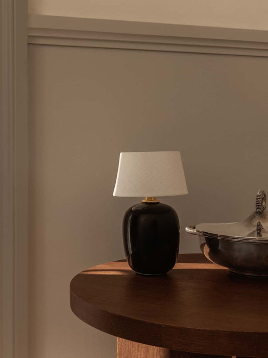 The black ceramic Torso Portable Table Lamp with a linen shade sits on a dark wood Androgyne Side Table in a softly lit room.