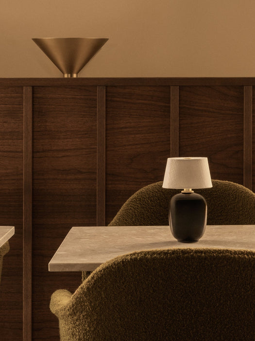 Black Torso Portable Table Lamp on a marble table between two bouclé Harbour Chairs. A brass Hashira Wall Lamp is behind.