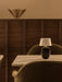 Black Torso Portable Table Lamp on a marble table between two bouclé Harbour Chairs. A brass Hashira Wall Lamp is behind.