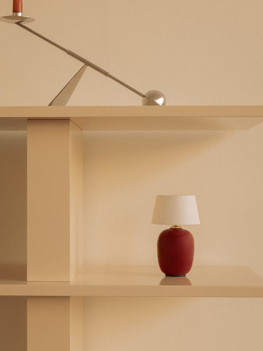The ruby Torso Portable Table Lamp sits on a beige shelf, with the chrome Interconnect Candle Holder on a shelf above.