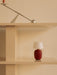The ruby Torso Portable Table Lamp sits on a beige shelf, with the chrome Interconnect Candle Holder on a shelf above.