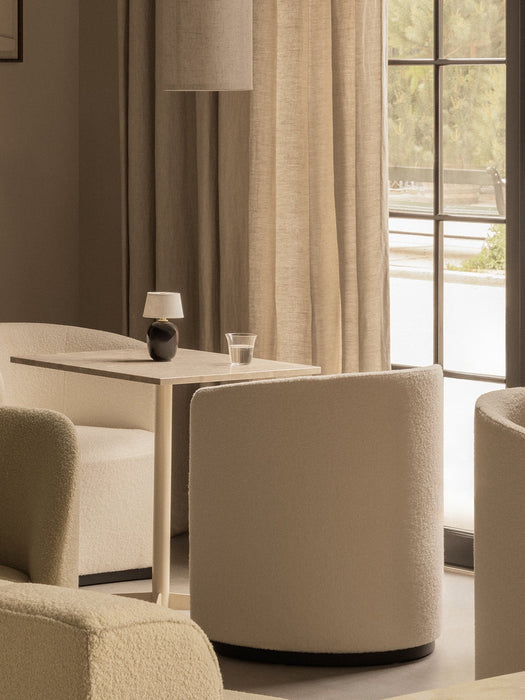 A portable Torso Table Lamp sits on a Nook Dining Table, placed between cream Tearoom Chairs in a cosy, softly lit interior.