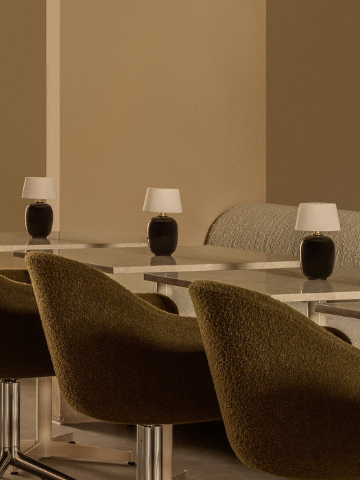 Three Torso Portable Table Lamps illuminate marble tables beside plush, green Harbour Dining Chairs in a modern interior.