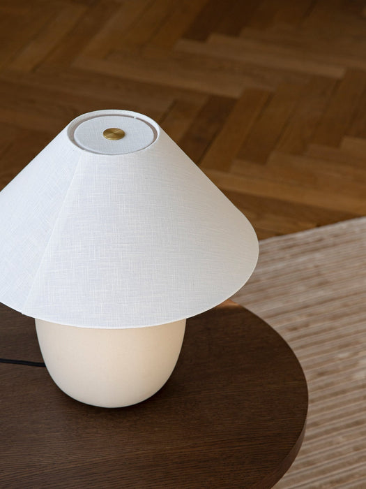 Close-up of the Torso Table Lamp, 37 showing the off-white linen shade and brass dimmer, placed on a dark wood table.