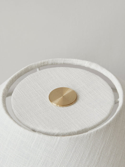 A close-up of the Torso Table Lamp, showing the textured off-white linen lampshade and the circular brass touch dimmer.