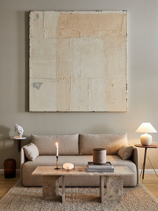 The Torso Table Lamp 37, lit on a side table next to a beige Offset sofa in a modern, minimalist living room setting.