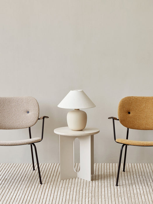 Torso Table Lamp on an Androgyne Side Table between a beige and a yellow Co Lounge Chair, set on a striped cream rug.