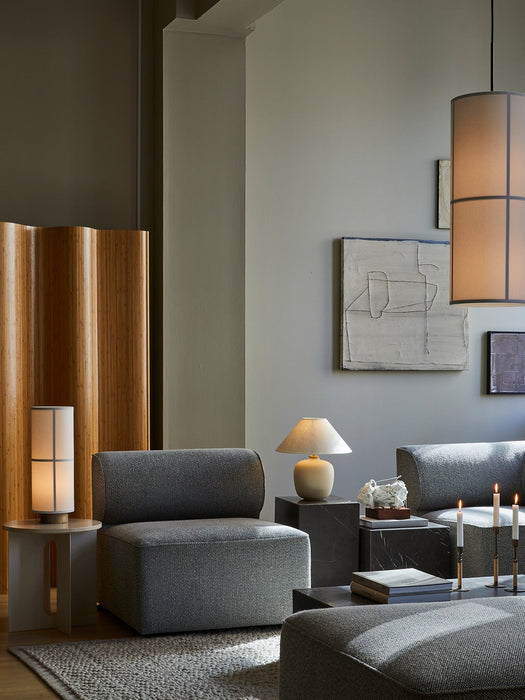 A modern living room featuring a grey Eave Sofa, with a beige Torso Table Lamp on a marble plinth and a Duca candelabra.