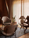 The Torso Table Lamp, 37 on a side table in a warmly lit living room with armchairs, a rug, and sheer curtains by a window.