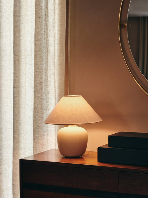 The Torso Table Lamp, 37, sits illuminated on a dark wood dresser beside two black boxes and a round gold mirror.