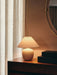The Torso Table Lamp, 37, sits illuminated on a dark wood dresser beside two black boxes and a round gold mirror.