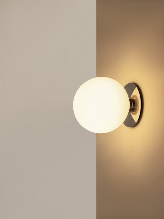 A close-up of the TR Bulb, Ceiling/Wall Lamp in polished steel, mounted in a corner, casting a warm glow on the walls.