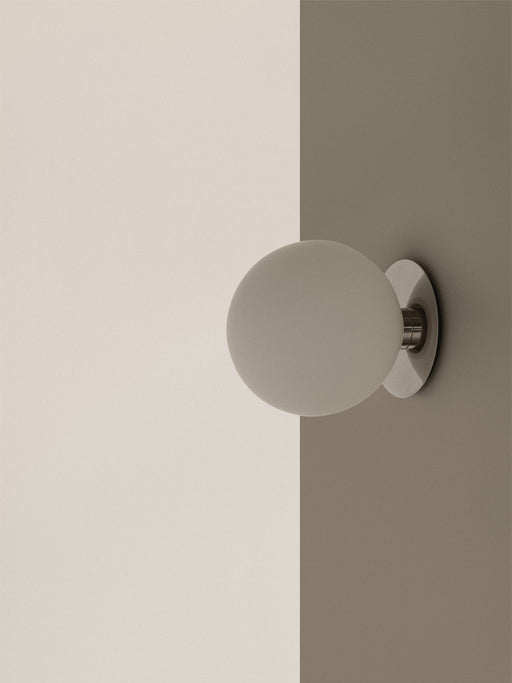 Close-up of the TR Bulb Ceiling/Wall Lamp in polished steel, its opal glass shade glowing against a two-toned wall.