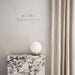 The TR Bulb lamp with its opal glass shade and brass base sits on a veined marble plinth against a light grey wall.