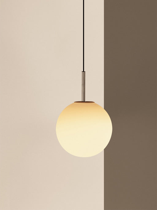 A close-up of the TR Bulb, Pendant, its spherical opal glass shade glowing warmly against a two-toned beige and brown wall.