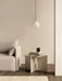 In a minimalist room, a TR Bulb Pendant hangs above an Androgyne Side Table with books, next to a beige Tearoom Sofa.