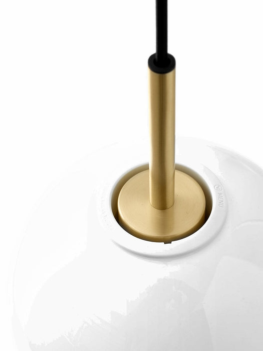 A close-up of the TR Bulb Pendant, showing the brushed brass fixture connecting the black cord to the white opal glass.