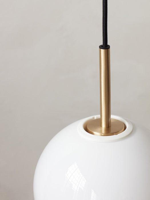 A close-up of the TR Bulb, Pendant light, detailing the brushed brass fixture emerging from the white opal glass globe.