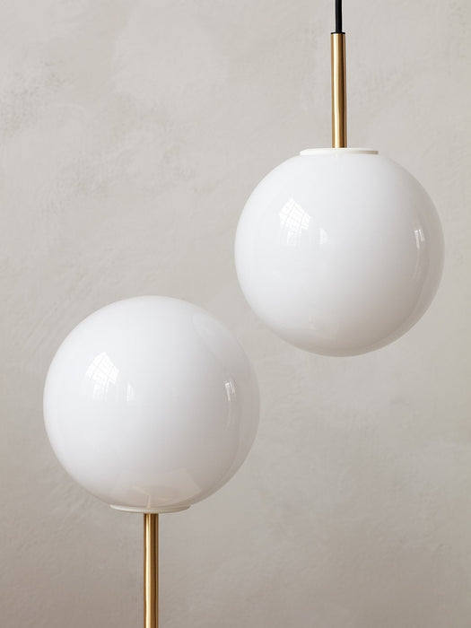 A close-up of the TR Bulb Pendant and Table Lamp with white opal glass shades and polished brass stems against a light wall.