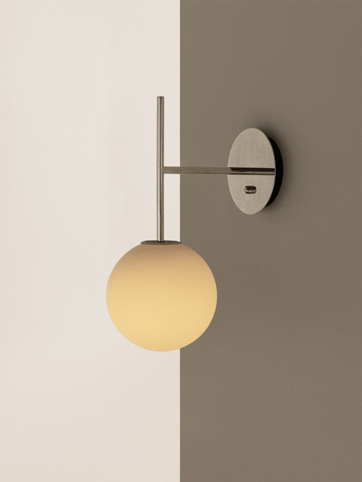 TR Bulb, Suspended Wall Lamp in polished steel, with a glowing opal glass bulb, on a two-toned white and taupe wall.