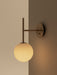 The TR Bulb Suspended Wall Lamp in brushed brass, featuring an opal glass bulb mounted on a corner of a beige and taupe wall.