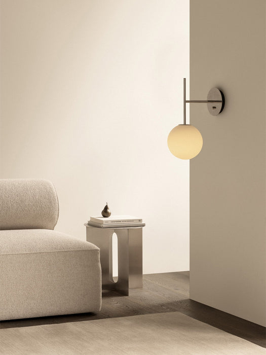 The TR Bulb Suspended Wall Lamp illuminates a corner with an Eave Modular Sofa and an Androgyne Side Table with a book.