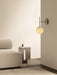 The TR Bulb Suspended Wall Lamp illuminates a corner with an Eave Modular Sofa and an Androgyne Side Table with a book.