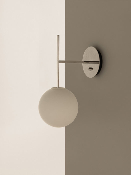 A close-up of the TR Bulb, Suspended Wall Lamp in polished steel, featuring an opal glass bulb, mounted on a two-toned wall.