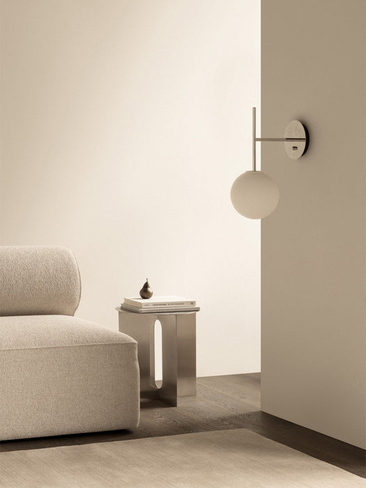TR Bulb Suspended Wall Lamp in polished steel on a wall beside an Eave sofa and an Androgyne side table in a calm setting.