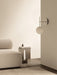TR Bulb Suspended Wall Lamp in polished steel on a wall beside an Eave sofa and an Androgyne side table in a calm setting.