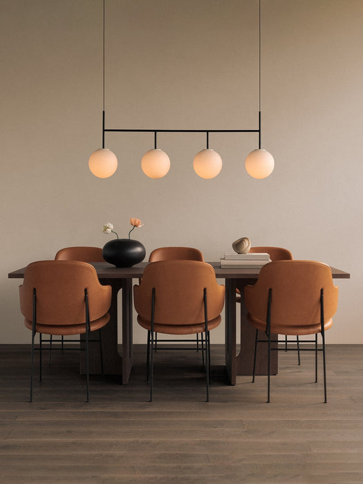 A TR Bulb Suspension Frame hangs over an Androgyne Dining Table with Penguin Dining Chairs. A black Surround Vase is on it.