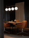 The TR Bulb Suspension Frame lights a Snaregade Oval Table and tan leather Harbour Swivel Chairs in a dimly lit, modern room.