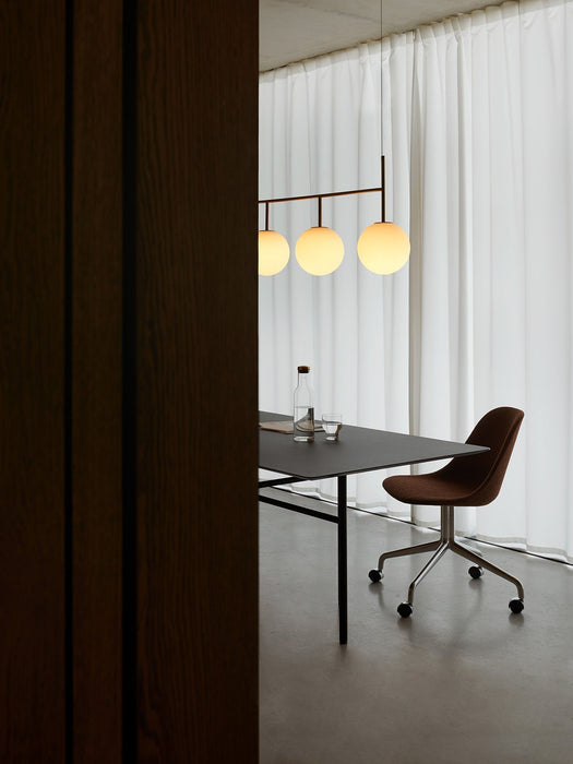 A TR Bulb Suspension Frame lamp hangs over a black dining table with a brown Harbour Side Chair in a minimalist room setting.