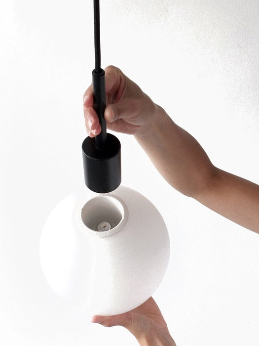 Close-up of hands installing a black light fitting into the large, spherical, white opal glass TR Bulb against a white wall.