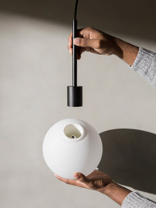 A person's hands assemble the TR Bulb light, inserting the black fitting into the spherical white opal glass shade.