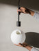 A person's hands assemble the TR Bulb light, inserting the black fitting into the spherical white opal glass shade.