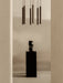 The Tubulaire Chandelier hangs above a black Collapse Vase which sits on a tall black marble Plinth in a minimalist room.