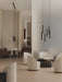 Two Tubulaire Chandeliers hang in a minimalist, modern lounge with beige and brown furniture, armchairs, a sofa, and stools.