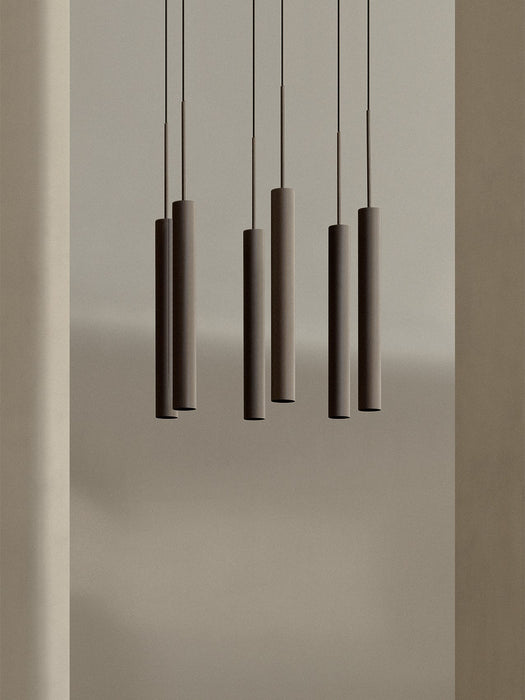 A close-up of the Tubulaire Chandelier, showing six reeded, bronzed brass pendant lights hanging against a neutral wall.