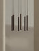 A close-up of the Tubulaire Chandelier, showing six reeded, bronzed brass pendant lights hanging against a neutral wall.