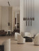 Modern room with a large Tubulaire Chandelier over a lounge with cream chairs and a Rail Pendant over a dining area.