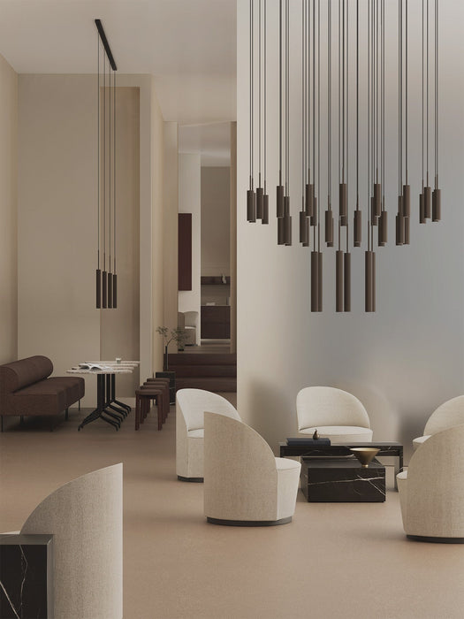 A large Tubulaire Chandelier with bronze pendants illuminates a modern lounge with cream armchairs and a black marble Plinth