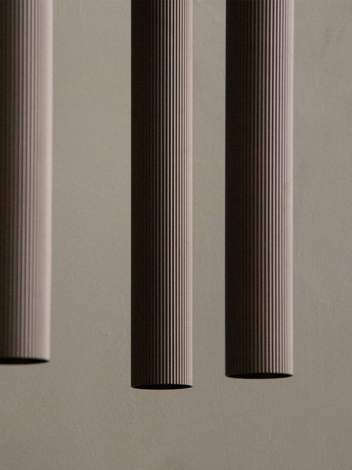 A close-up of three Tubulaire Pendant Lamps showing the reeded texture of the bronzed brass aluminium against a grey wall.