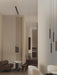 A Tubulaire Rail Pendant illuminates a minimalist dining area with a brown sofa and stools, in a softly lit, neutral room.