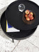 A black Turning Table, its top rotated to show a magazine in storage. On top is a bowl of apples and a glass orb.